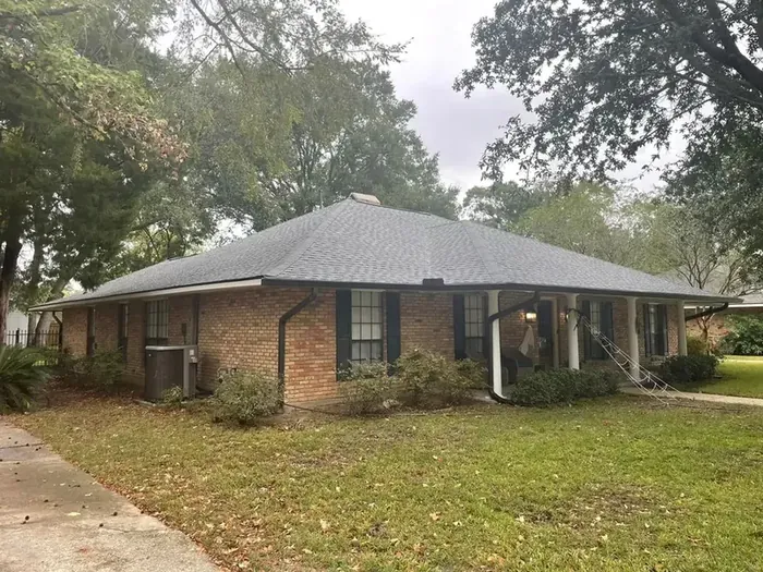 Front elevation of a brick ranch home under oaks, gutter run and downspout visible along the eave